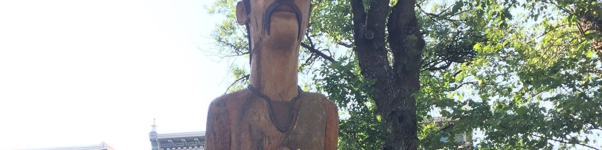 Una estatua de un hombre con sombrero y botas, rodeada por un borde de ladrillo y una placa.