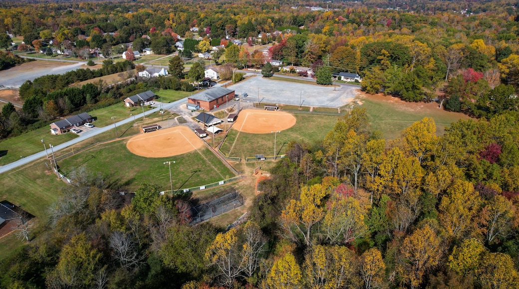 An aerial view of a baseball field surrounded by autumn-colored trees and residential houses.