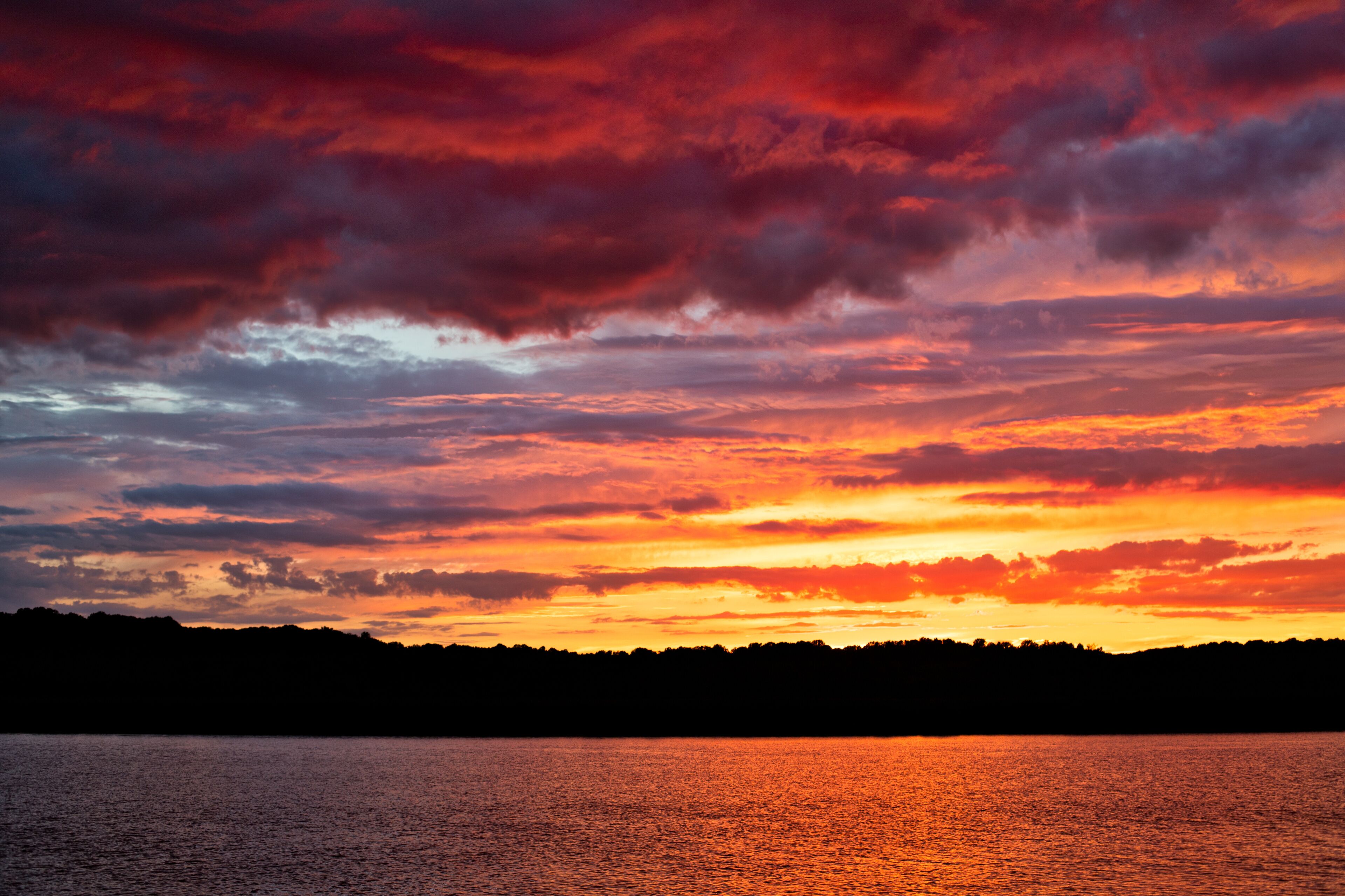 A sunset over a body of water with a silhouette of a forested shoreline.