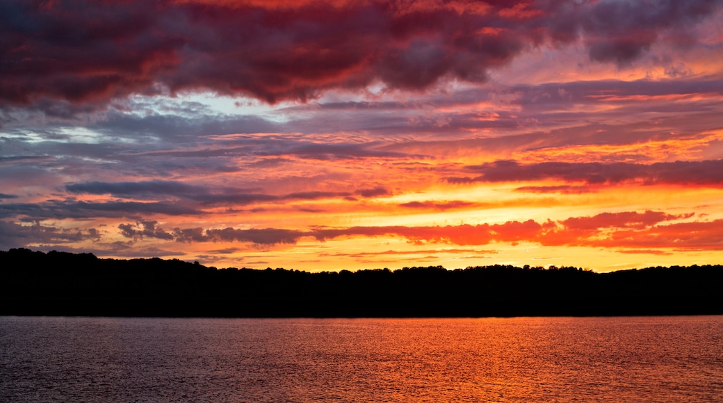 A sunset over a body of water with a silhouette of a forested shoreline.