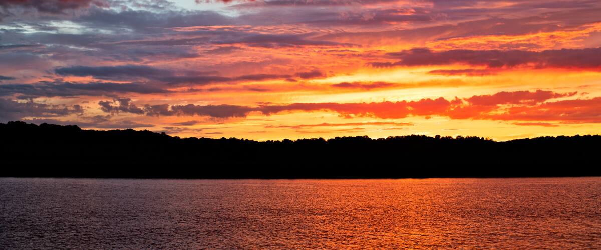 A sunset over a body of water with a silhouette of a forested shoreline.
