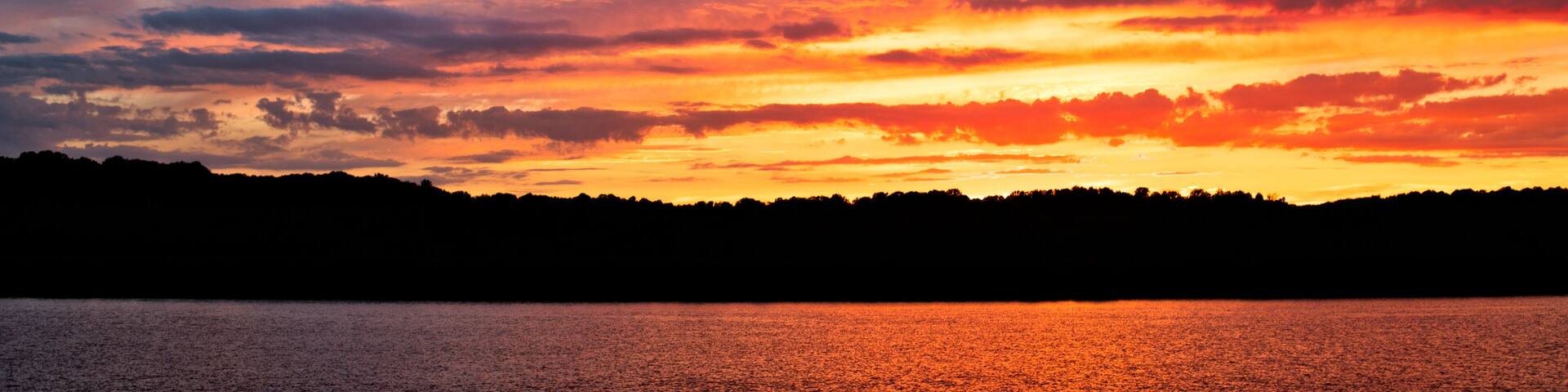 A sunset over a body of water with a silhouette of a forested shoreline.