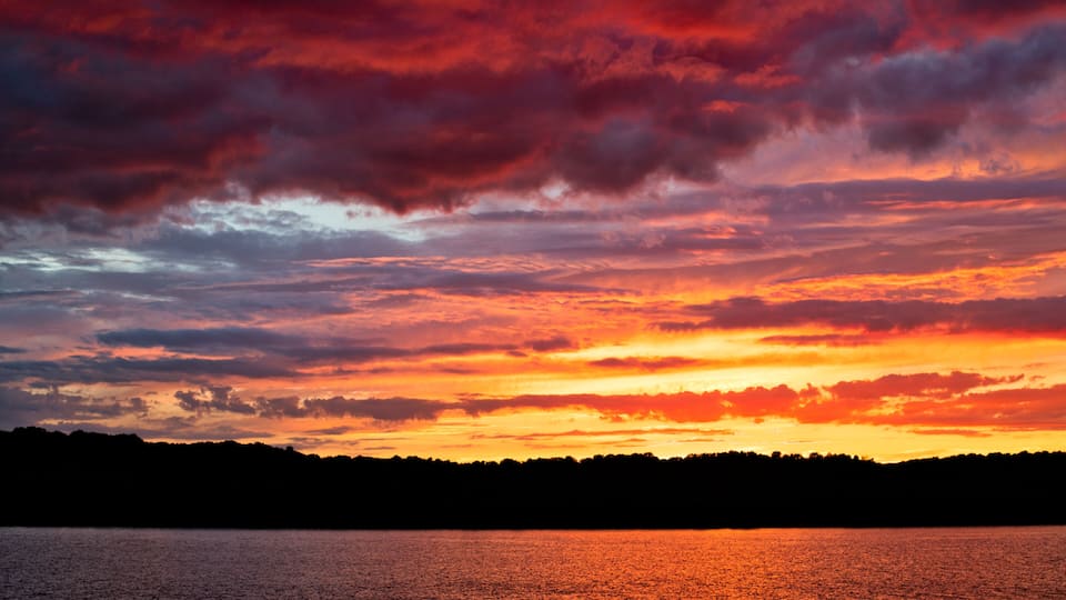 A sunset over a body of water with a silhouette of a forested shoreline.