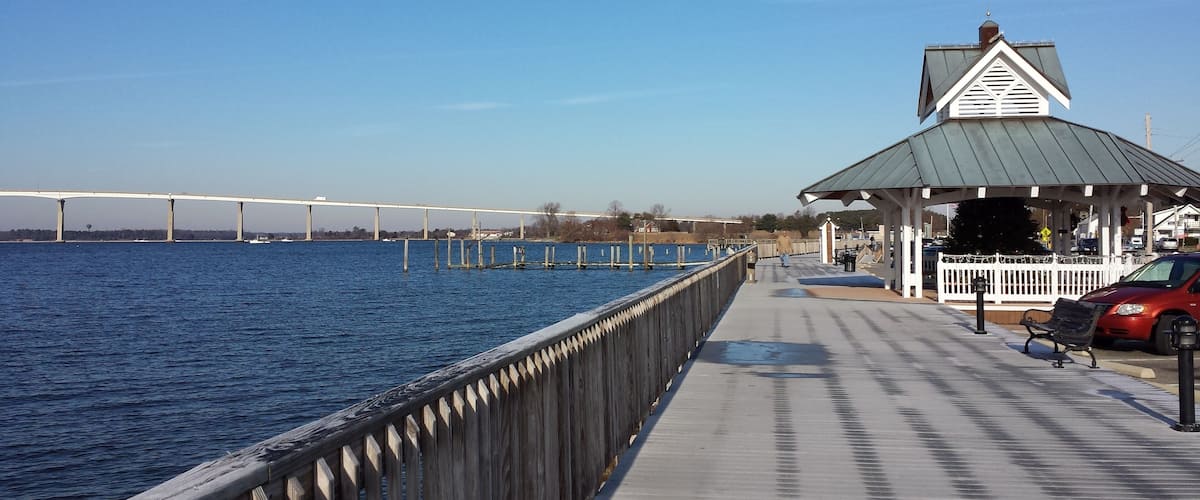 A wooden pier extending into a body of water with a bridge in the background.