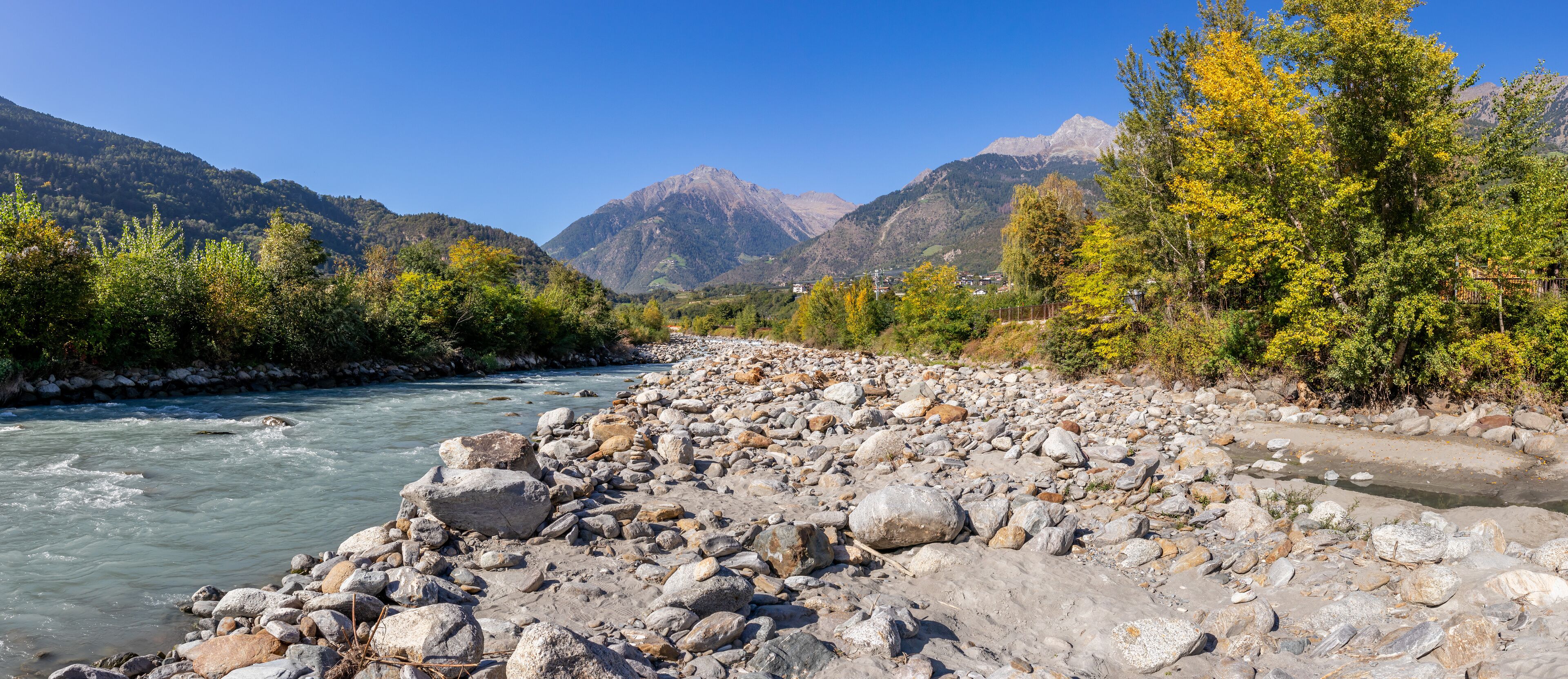 A river with rocky banks, surrounded by mountains and autumn-colored trees.