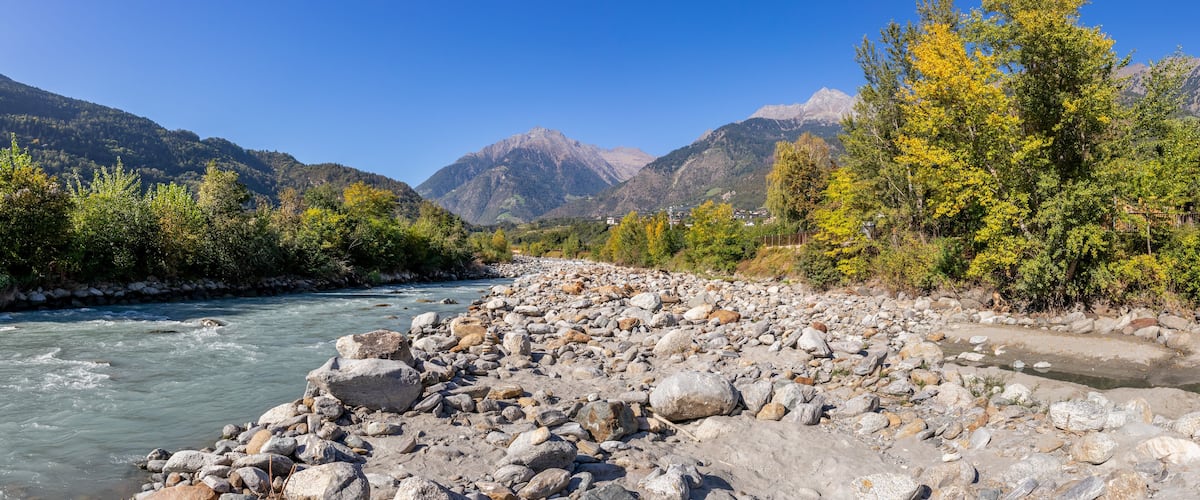 A river with rocky banks, surrounded by mountains and autumn-colored trees.