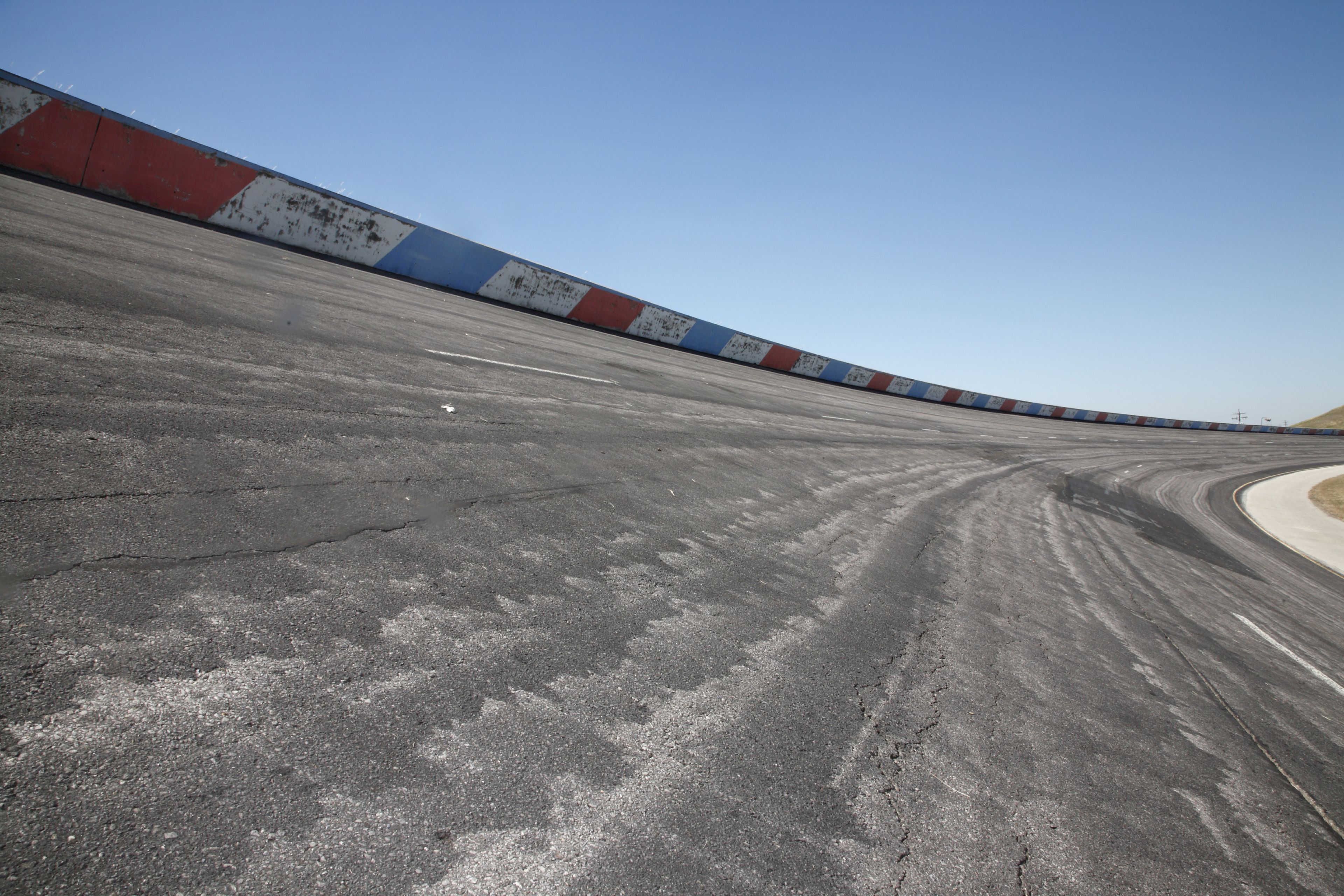 A curved racetrack with a concrete surface and a colorful barrier.