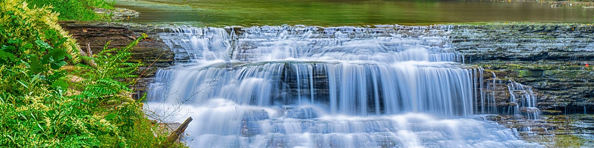 Una cascada que se precipita sobre un saliente rocoso rodeado de abundante vegetación.