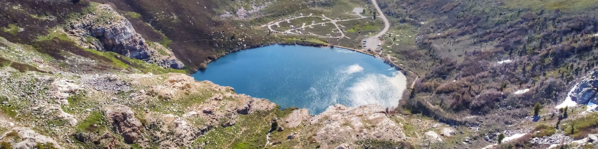 A mountainous landscape with a lake, winding roads, and sparse vegetation.