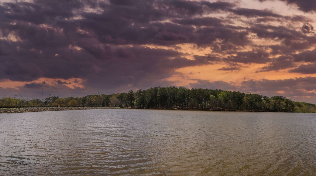 a panoramic shot of a vast rippling lake surrounded by lush green trees with powerful red clouds at sunset at Murphey Candler Park in Atlanta Georgia USA