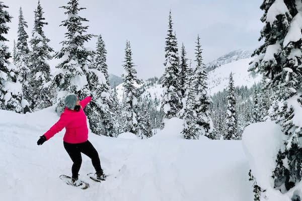 Eine Person snowboardet durch einen verschneiten Wald mit hoch aufragenden Nadelbäumen.
