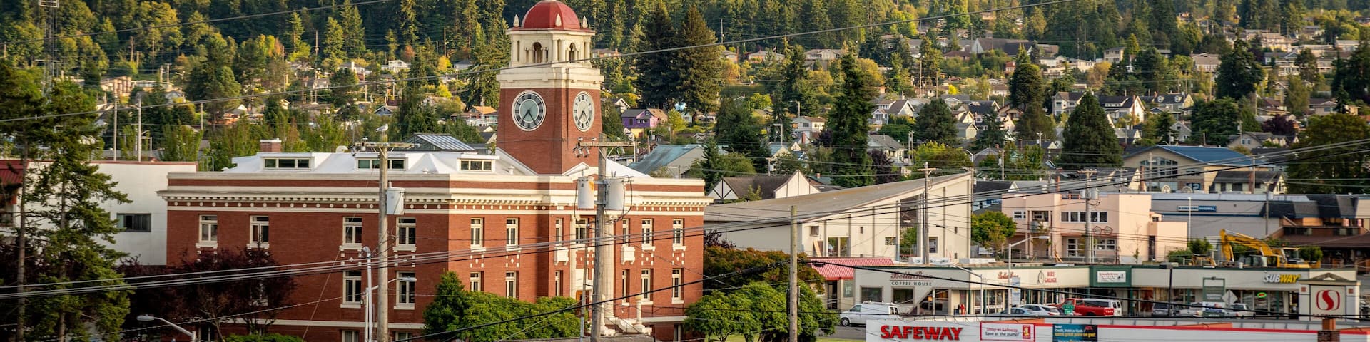 A town with a prominent clock tower, a Safeway store, and a mountainous backdrop.
