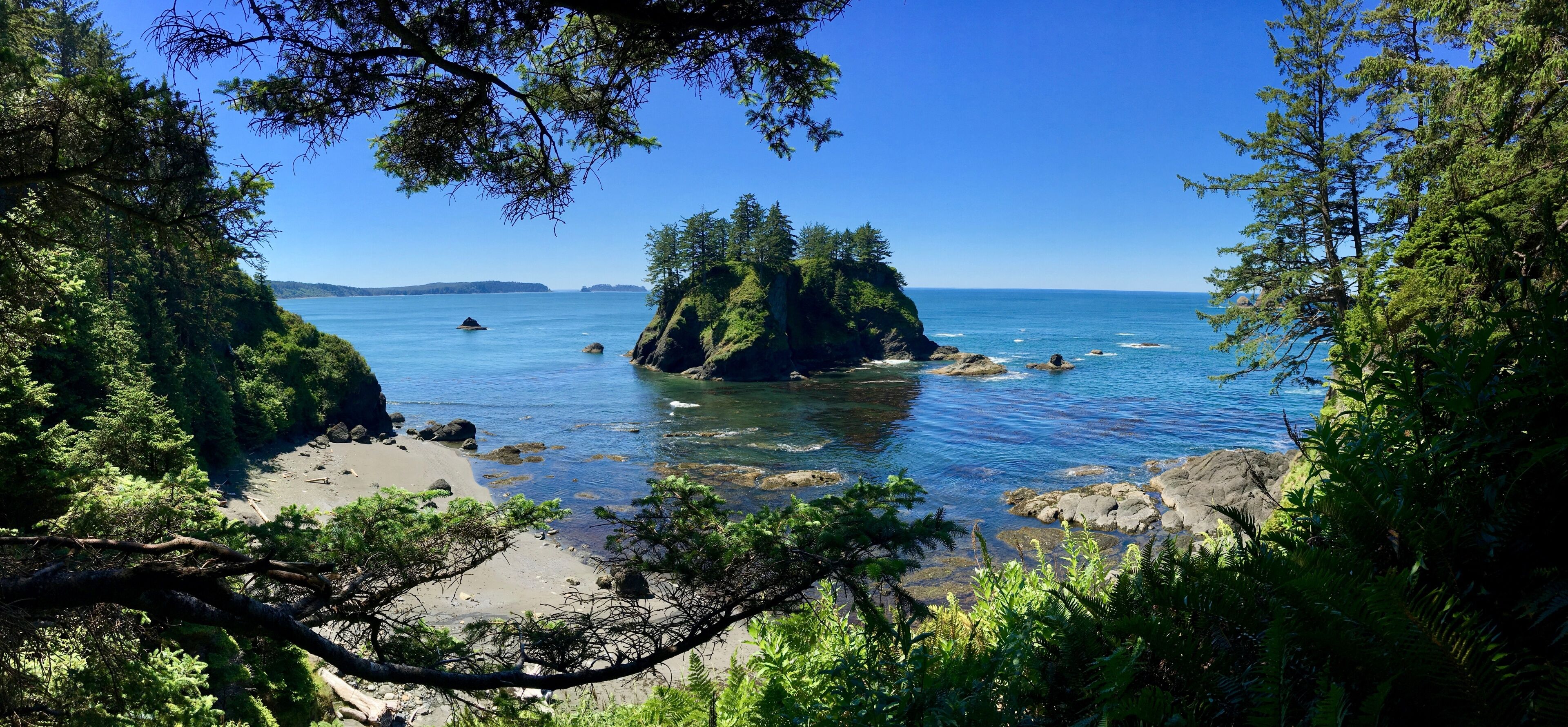 A coastal landscape with a prominent rock formation surrounded by dense greenery and clear blue waters.