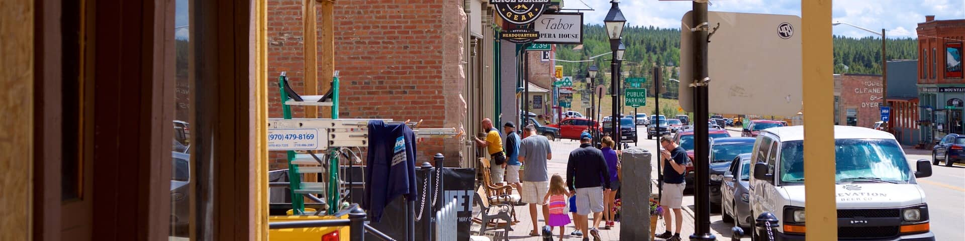 A bustling street with a vintage building, a sign for Genuine Race Series Gear, and a public parking sign.
