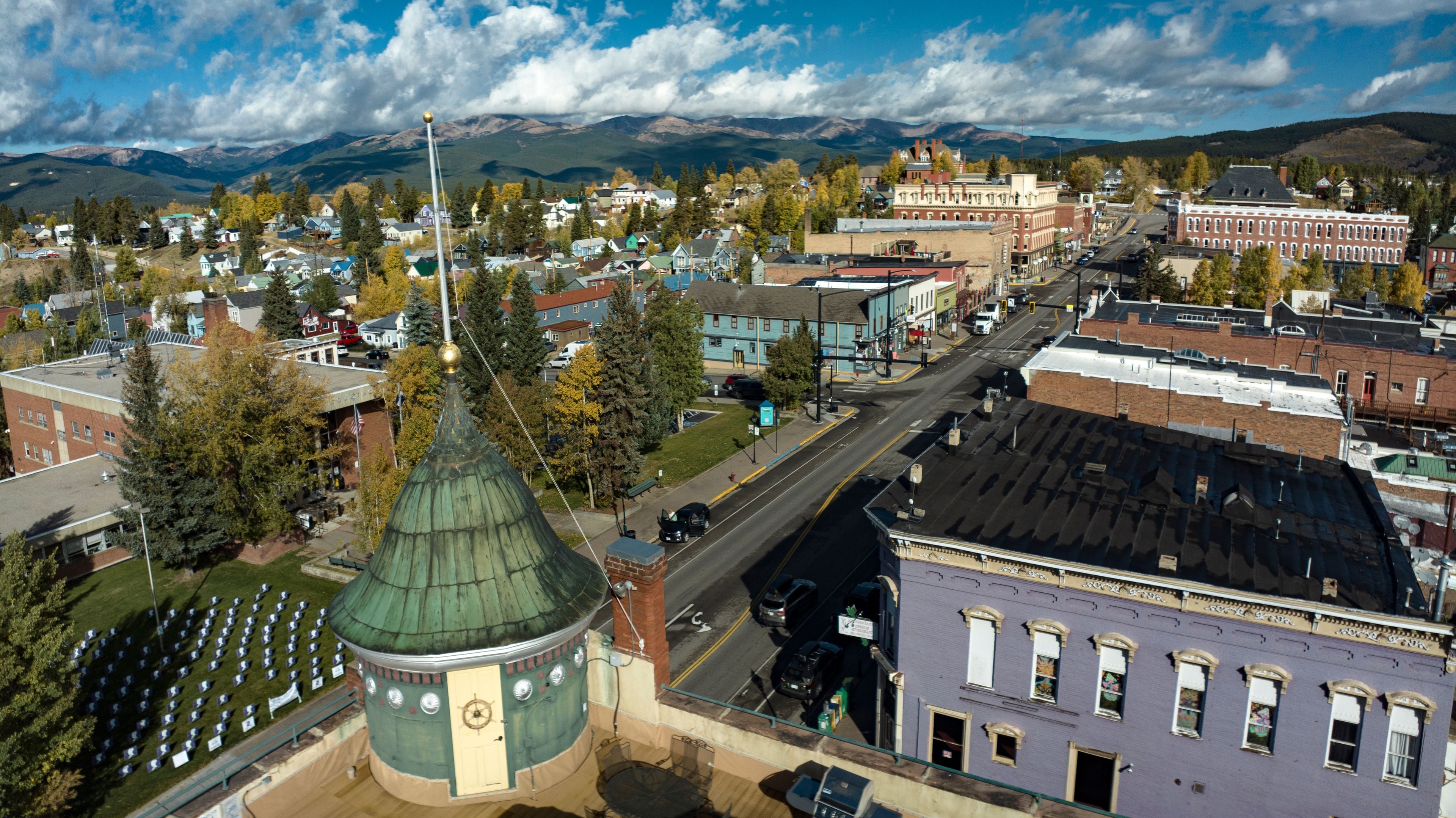 A town with a distinctive green-roofed building, a river, and mountains in the background.