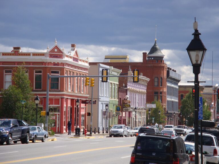 A street lined with historic buildings, a traffic light, and cars on a sunny day.