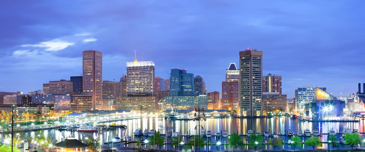 A city skyline at dusk with illuminated buildings and a river with boats.