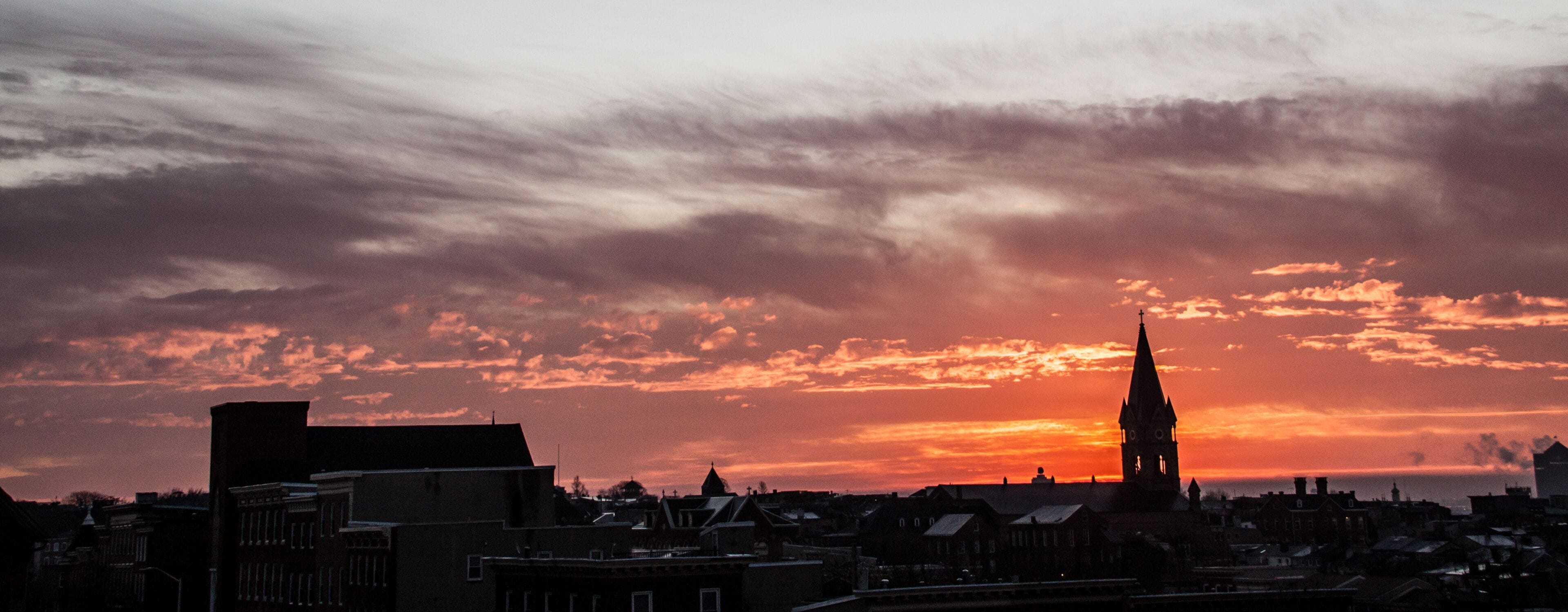 dramatic sunrise of the Baltimore skyline with a church steeple on the foreground.