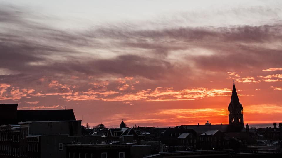 A city skyline at sunset with a prominent church spire silhouetted against a vibrant sky.