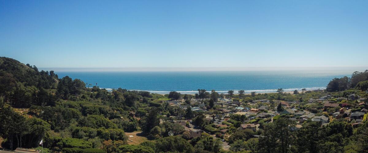 A coastal town with dense greenery, a clear blue sea, and a hilly backdrop.
