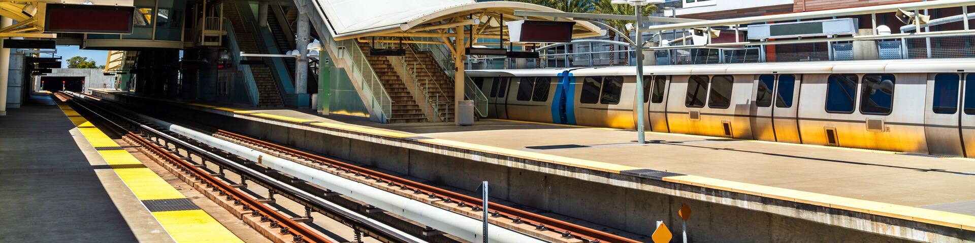 View of the platforms and modern architectural design of the Millbrae Transit Station with a bart train and urban housing near San Francisco in California, United States