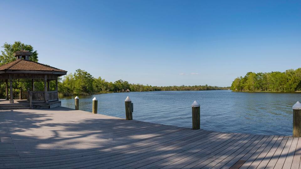 A wooden pier with a gazebo and bollards, leading to a calm lake surrounded by trees.