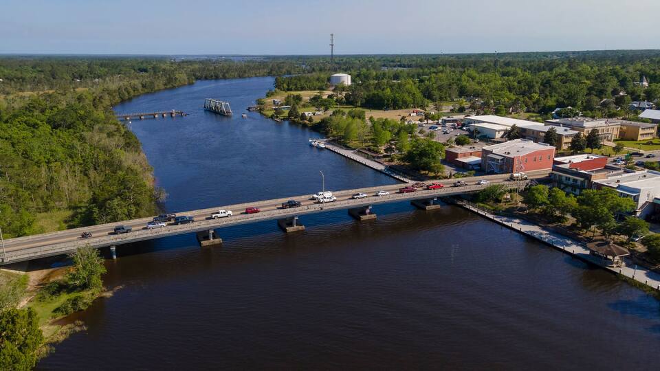A river with a bridge, a dock, and buildings along the riverbank.