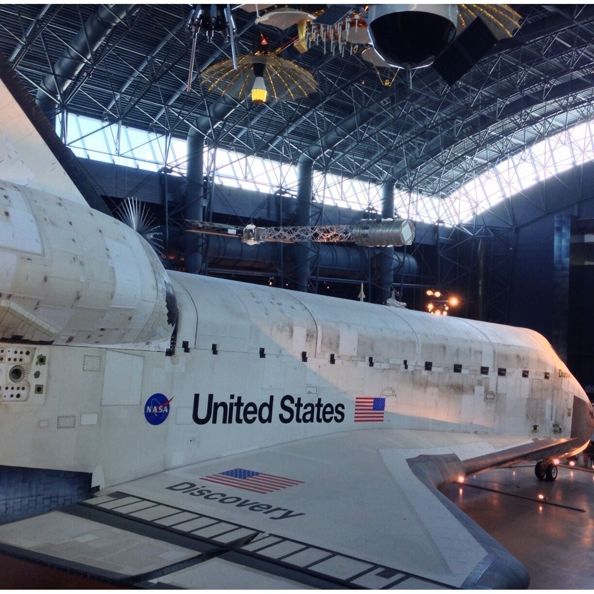 A space shuttle with NASA and United States logos, inside a large hangar.