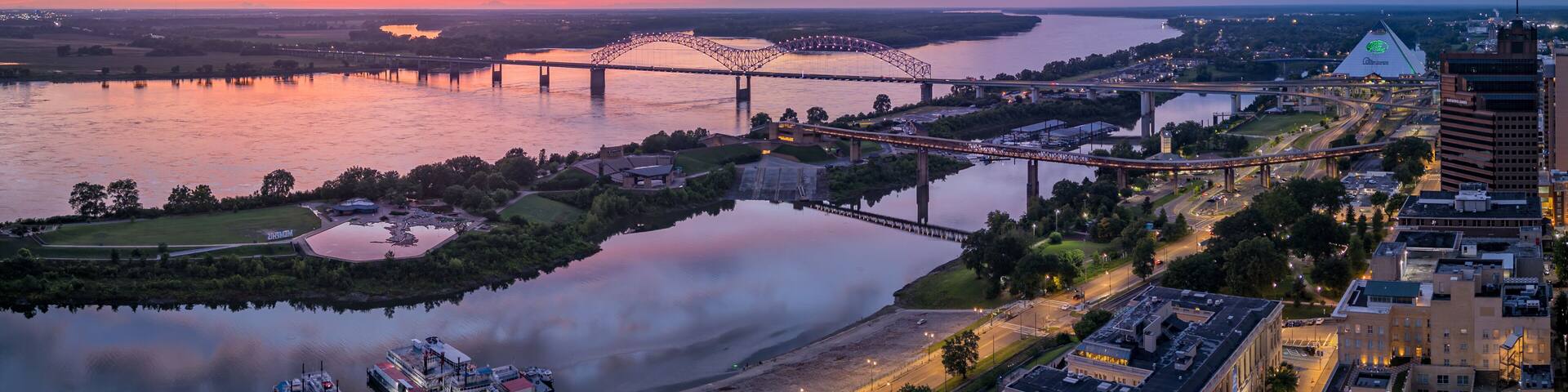 A sunset over a river with bridges, a boat dock, and urban buildings.
