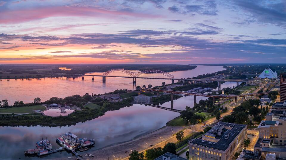 A sunset over a river with bridges, a boat dock, and urban buildings.