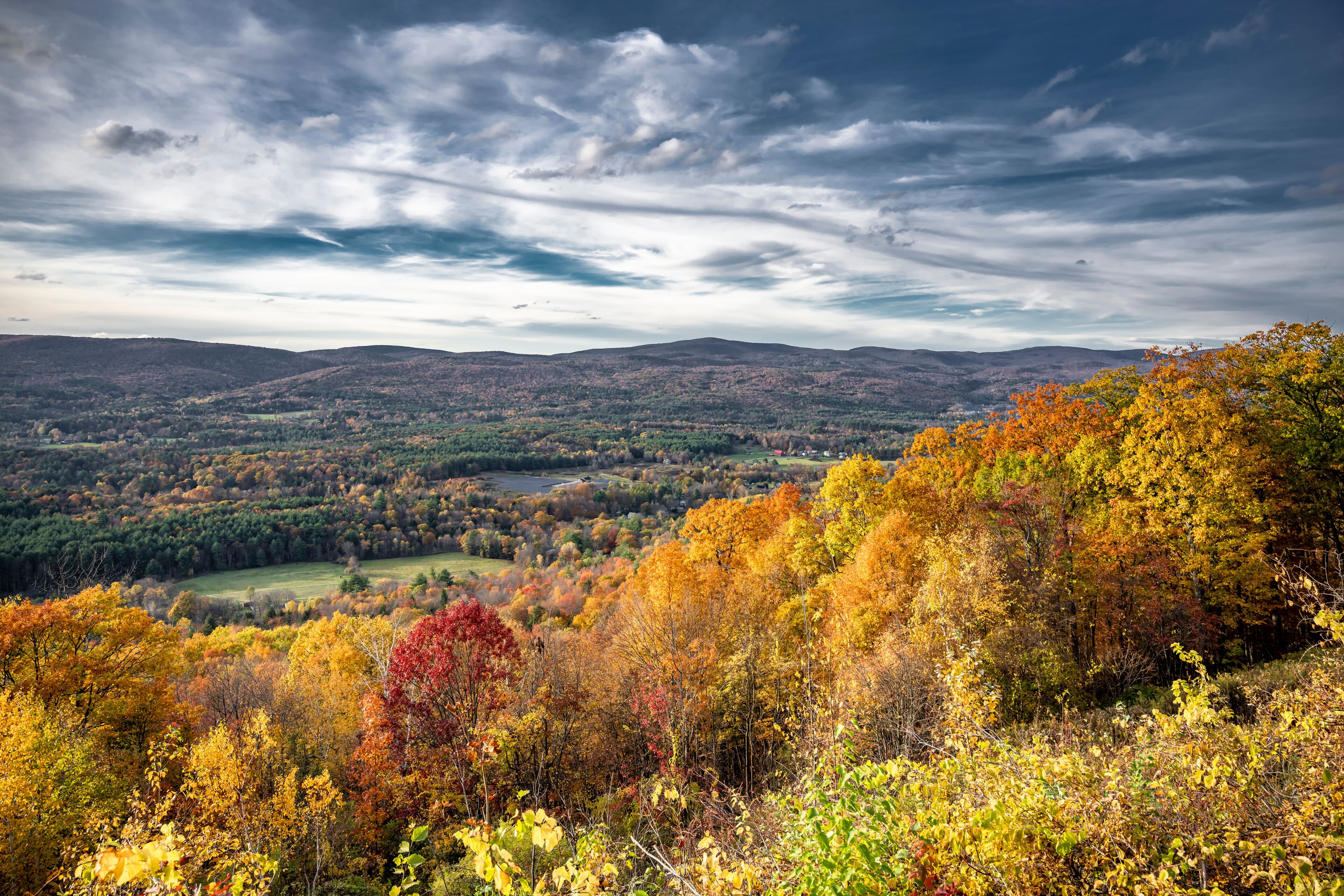 Scenic Autumn Maple Grove and Valley City in Sunlight and Thunderstorm Skies in the rolling hills of Vermont