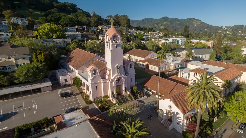 A church with a bell tower, surrounded by residential buildings and palm trees.
