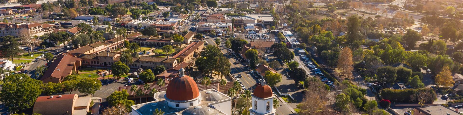 An aerial view of a town with a prominent church featuring two domes, surrounded by residential areas and a hilly landscape in the background.