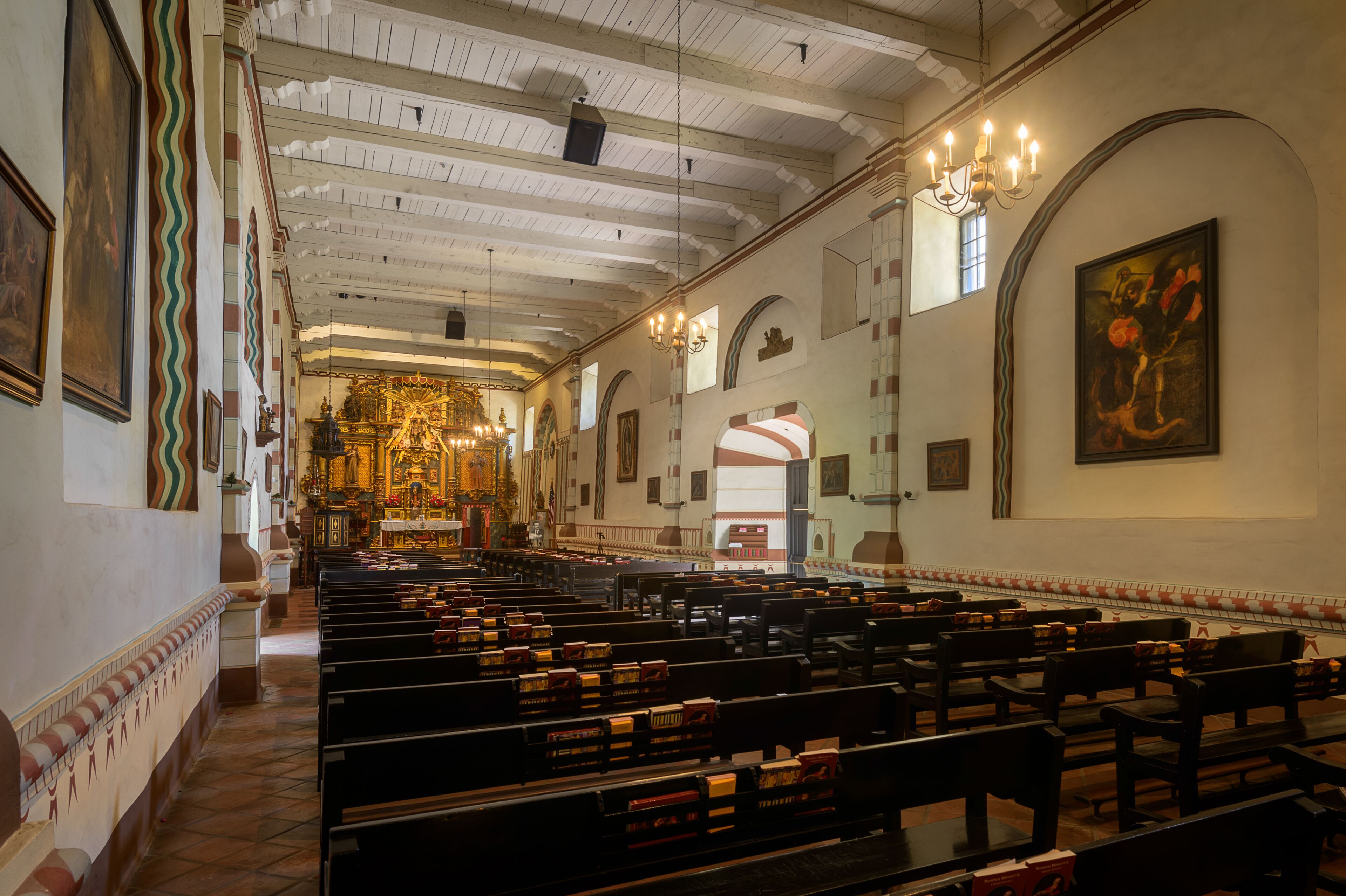 An interior of a church with pews, a chandelier, and religious artwork.
