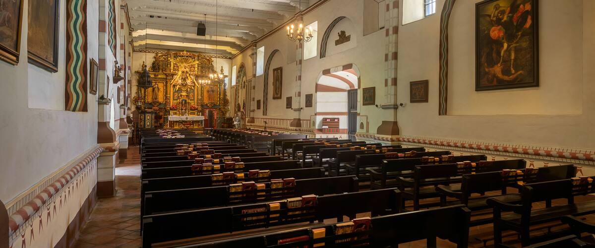 Interior de una iglesia con bancales, una araña de cristal y arte religioso.