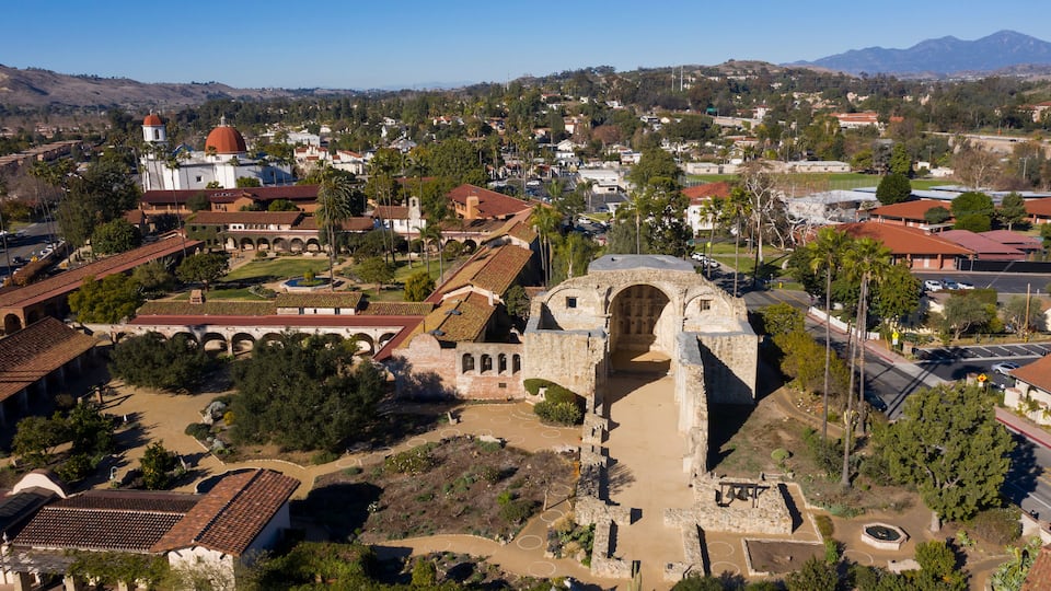 An aerial view of a historic site with a prominent archway, surrounded by traditional buildings and palm trees.