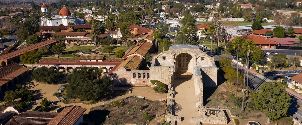 An aerial view of a historic site with a prominent archway, surrounded by traditional buildings and palm trees.