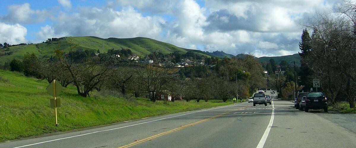 A road with a speed limit sign of 35, surrounded by green hills and a partly cloudy sky.