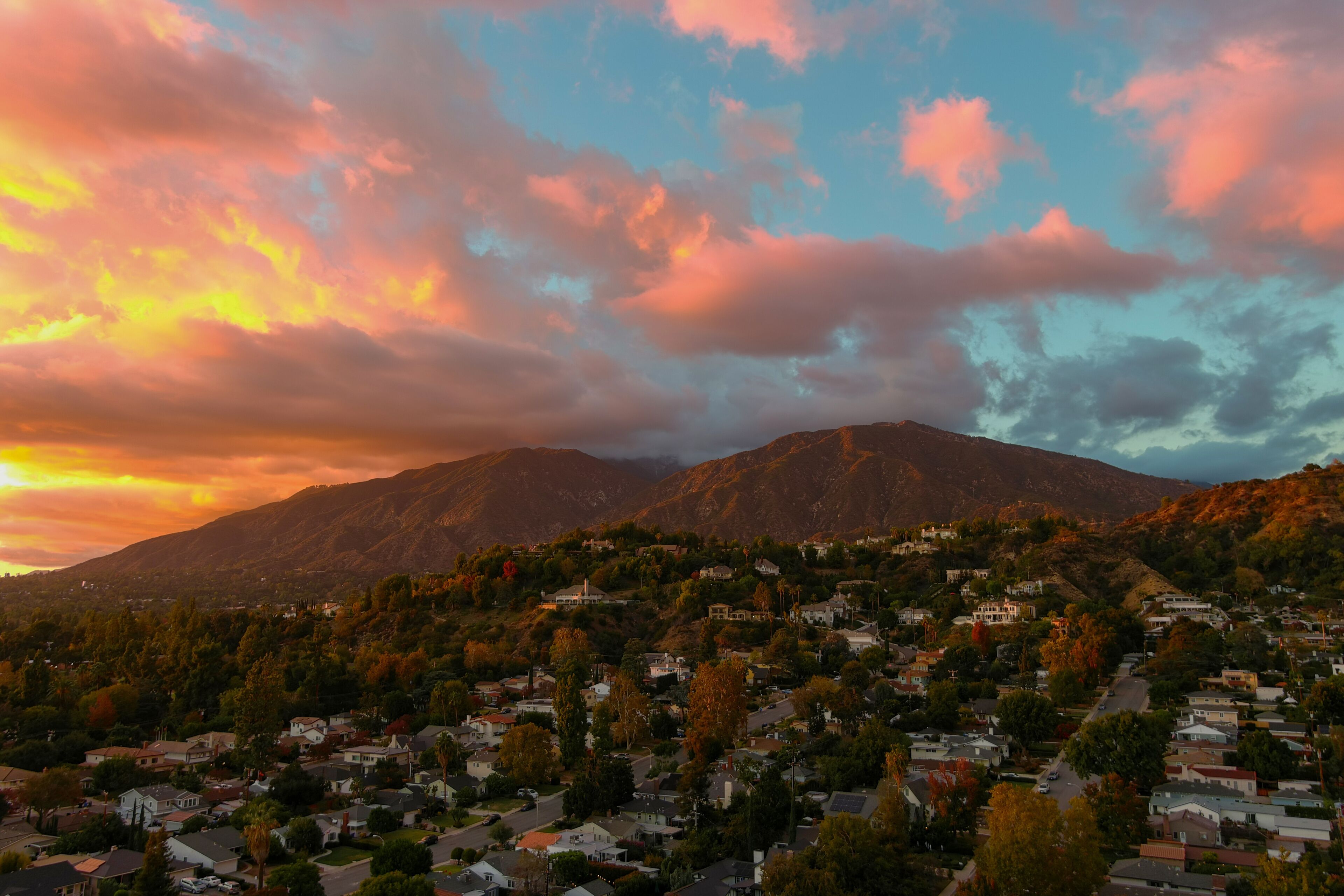 aerial shot of majestic mountains with powerful clouds and blue sky with homes, apartments and lush green trees at sunset in Monrovia California USA