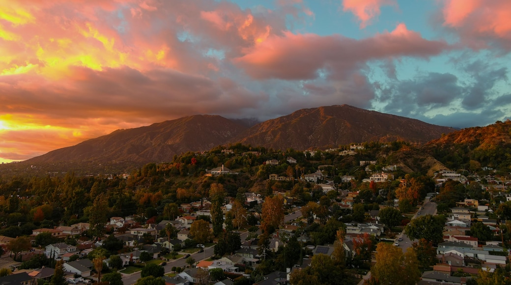 aerial shot of majestic mountains with powerful clouds and blue sky with homes, apartments and lush green trees at sunset in Monrovia California USA