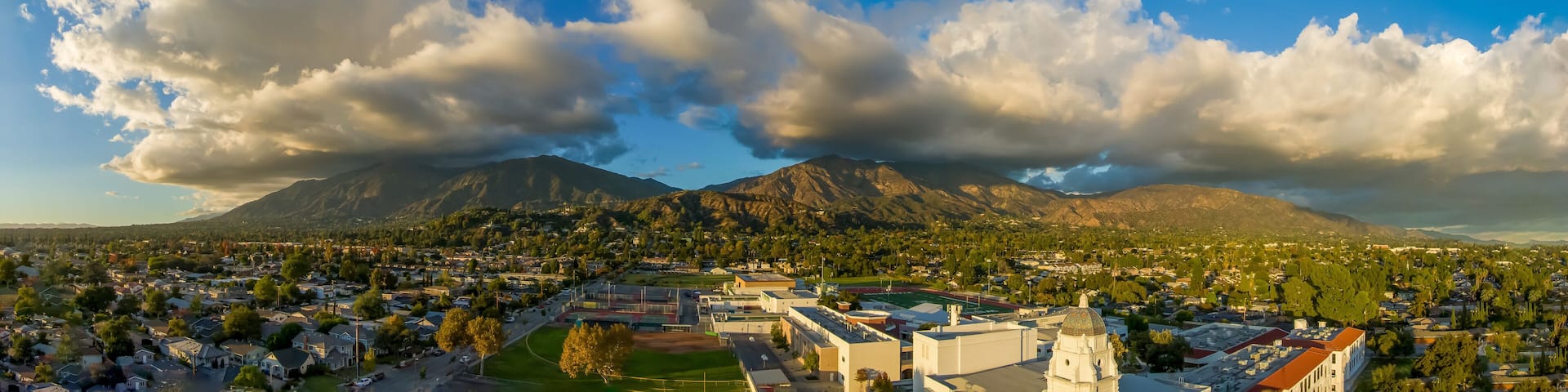 aerial shot of homes, apartments, and shops in the city skyline with cars driving on the street lush green trees at sunset in Monrovia California USA