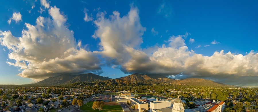 aerial shot of homes, apartments, and shops in the city skyline with cars driving on the street lush green trees at sunset in Monrovia California USA