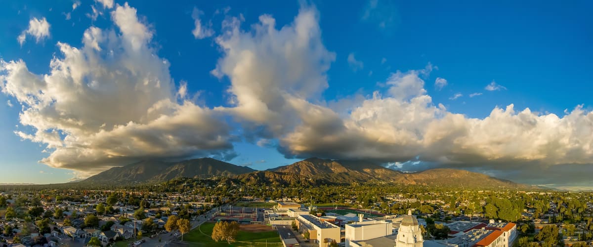 A town with a mountain range in the background, a clear sky, and scattered clouds.