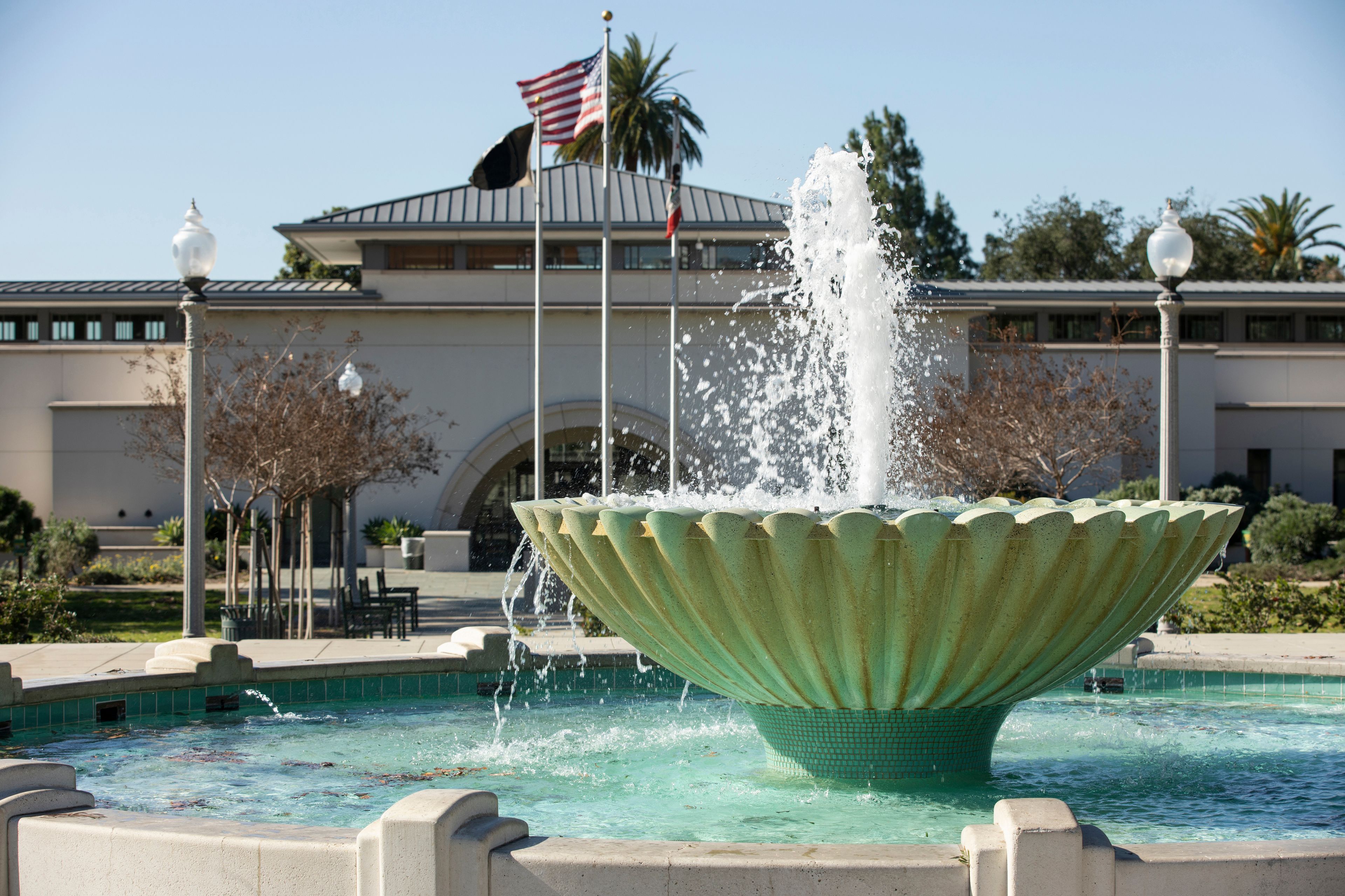 A fountain with water jets in a pool, surrounded by a building with an American flag.
