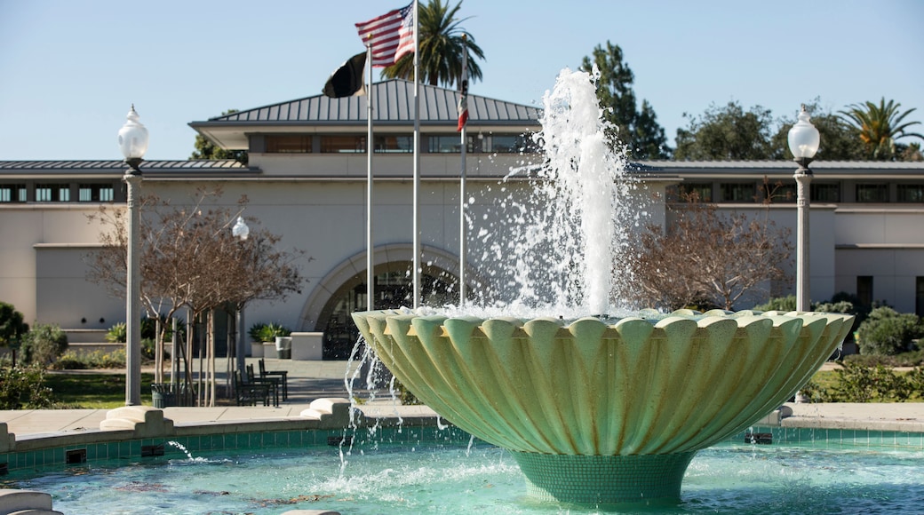 A fountain with water jets in a pool, surrounded by a building with an American flag.