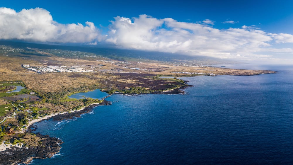 An aerial view of a coastal landscape with a clear sky, a large body of water, and a small island with buildings.