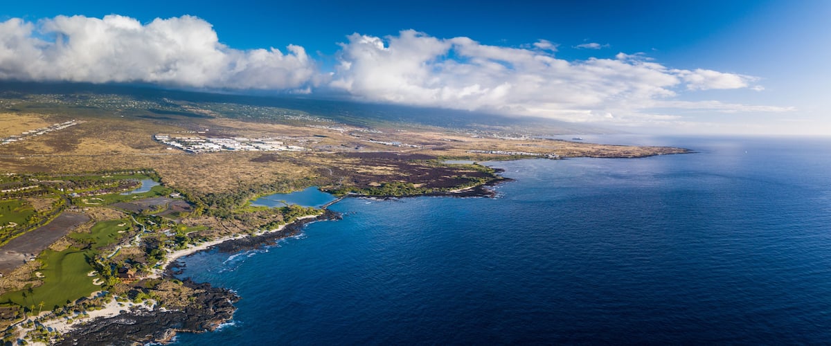 Une vue aérienne d’un paysage côtier, avec un ciel dégagé, une vaste étendue d’eau et une petite île abritant des bâtiments.