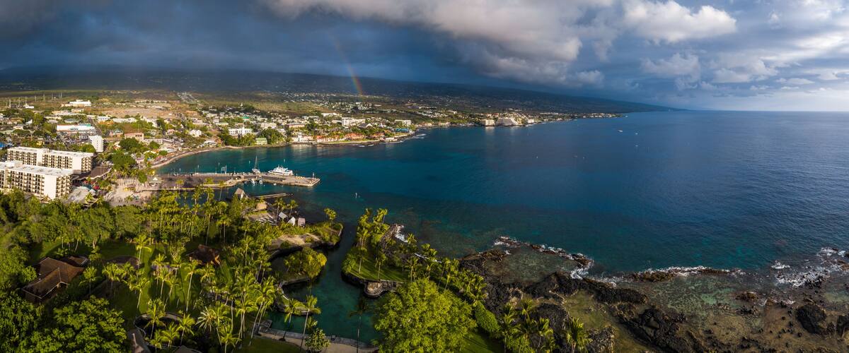A coastal cityscape with a clear view of the ocean, a marina, and a rainbow.