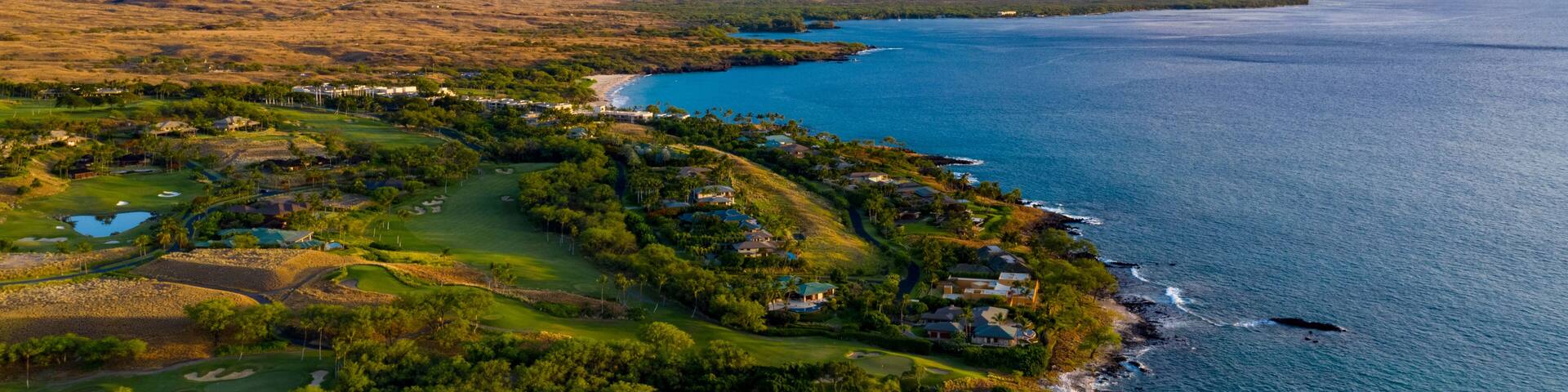 A coastal landscape with a golf course, beach, and ocean.