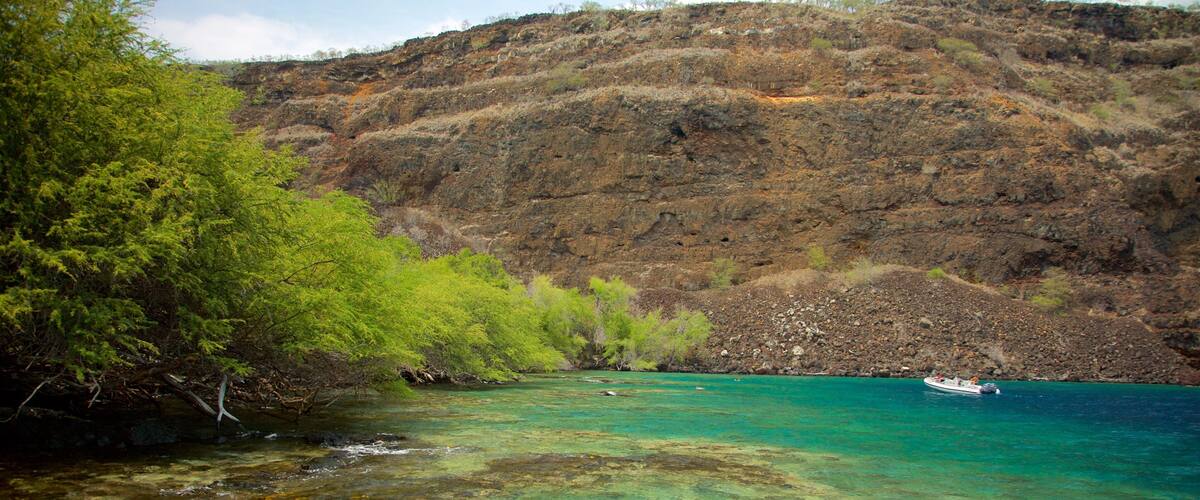 A coastal landscape with clear turquoise waters, rocky cliffs, and green vegetation.